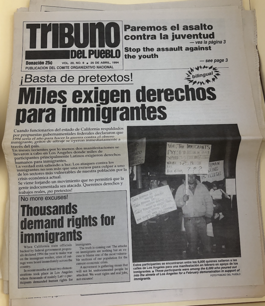 ○	An old newspaper shows a text box on the left hand side with a bold title reading “Tribuno del Pueblo”. There are two bold, small headlines next to the text box in English and in Spanish. There is a bold headline in Spanish below along with text. On the right hand side, there is an image of people standing, holding protest signs in black and white. On the bottom left hand corner, there is a gray textbox with a a bold headline and a paragraph in English. 