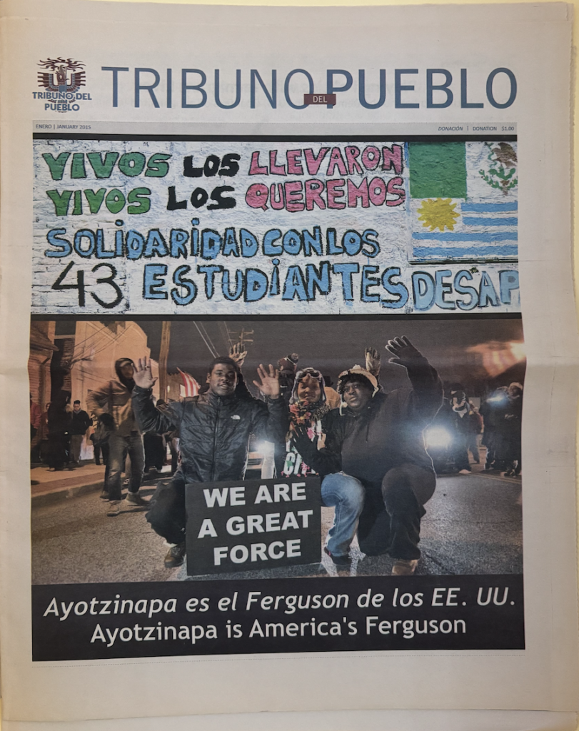 ○	A colorful newspaper shows a small logo on the top left corner with a phoenix rising. The title of the paper is in thin, blue letters that read Tribuno del Pueblo. There are two images on the paper with the top one showing a drawing. The drawing has a blue background with letters in green, black, red, and light blue that reads “Vivos los llevaron, vivos los queremos. Solidaridad con los 43 estudiantes desap-”. On the right side of the drawing there are two flags showing the Mexican flag and Uruguayan flag. The image below shows a group of people at night, kneeling, and with their hands up. A black sign with white letters reads “We Are A Great Force”. There is a black textbox with white letters showing two headlines, one in Spanish and one in English. 